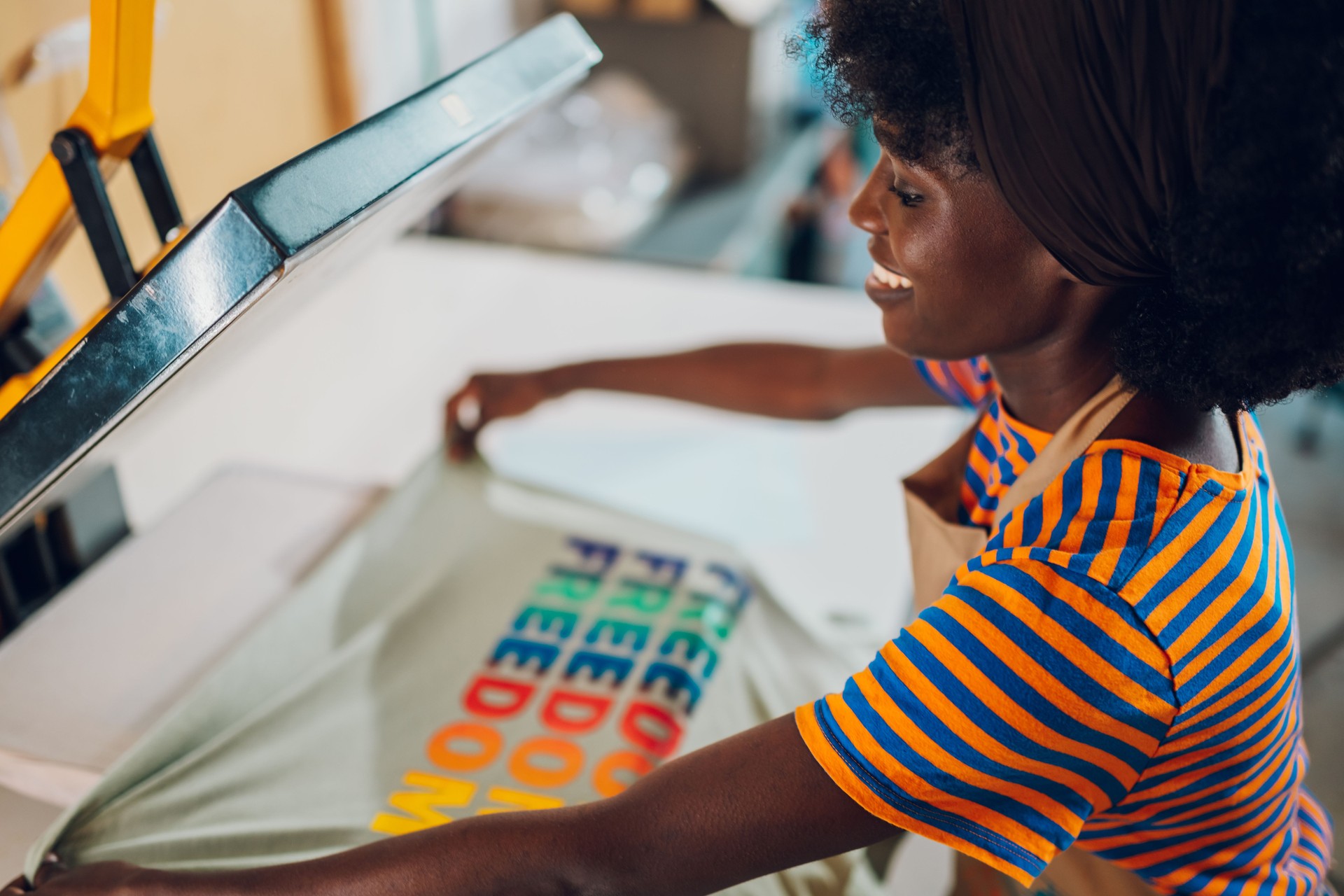 Interracial worker putting t-shirt on heating press at printing shop.